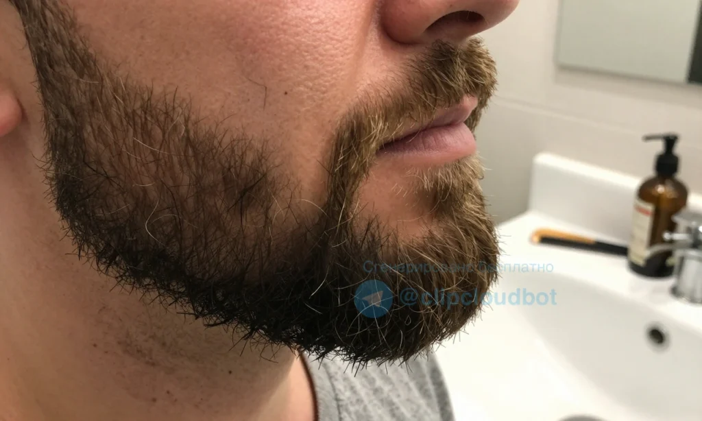 A close-up of a well-groomed beard with visible split ends at the tips, showing dry, frayed hairs under soft natural lighting, with a subtle background of a bathroom sink and grooming tools like a beard oil bottle and comb nearby, emphasizing hair texture and care without any shortening or cutting action